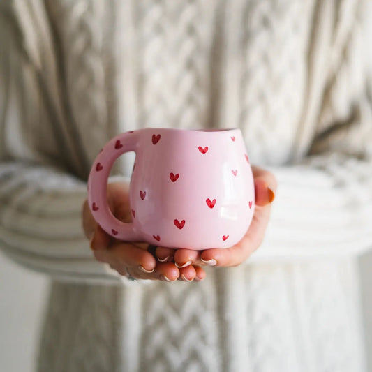 tasse rose avec coeurs rouges entre les main d'une femme