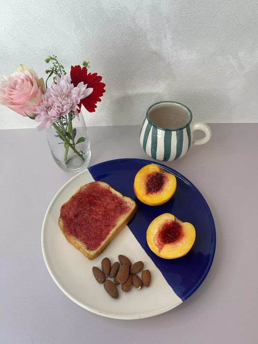 scène de petit déjeuner avec vase, fleurs, assiette bicolore en céramique artisanal et tasse colorée 