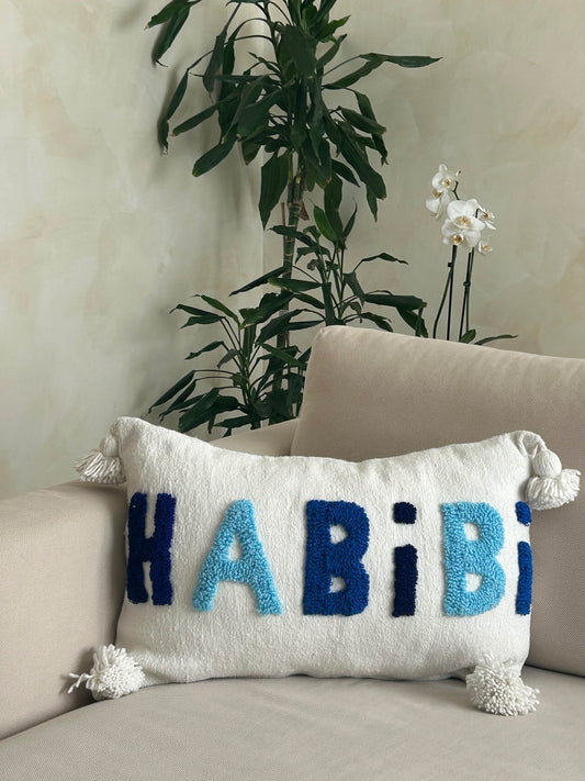 housse de coussin artisanale en laine blanche et pompons, motif Habibi dans un dégradé de bleus 